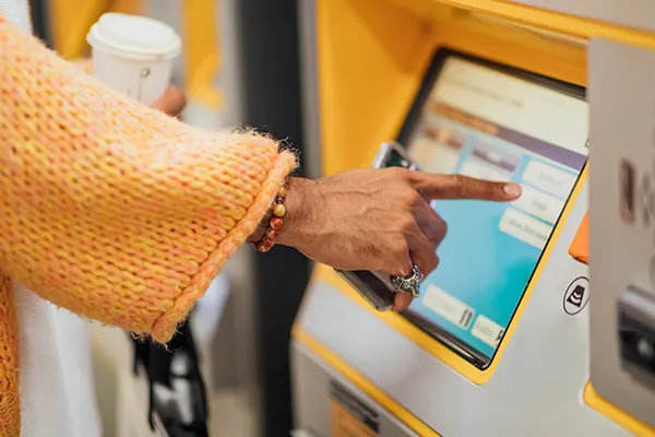 A hand reaching out to press the touch screen of a ticket machine at a train station
