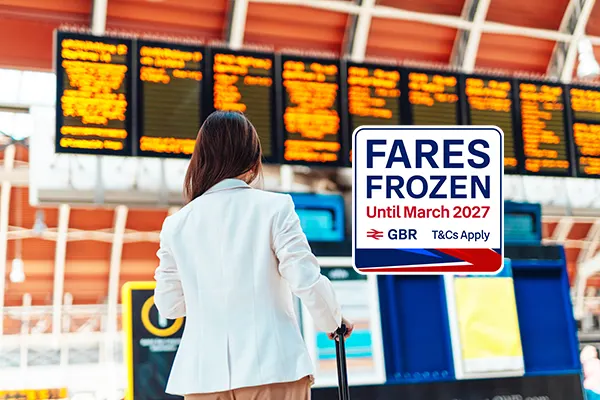Person in white jacket looking at departure board with yellow text displays at railway station. A badge is over the image, which says FARES FROZEN UNTIL MARCH 2027.
