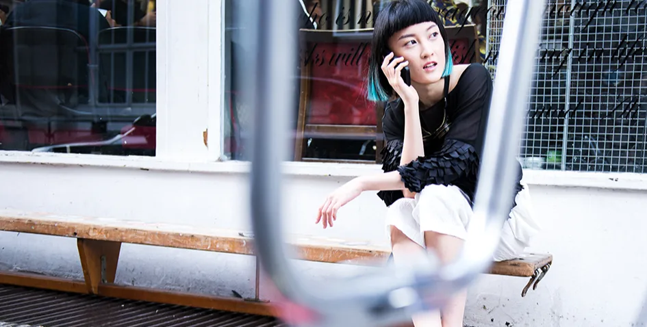 A fashionable young woman sits on a bench outside a shop making a call on a mobile phone