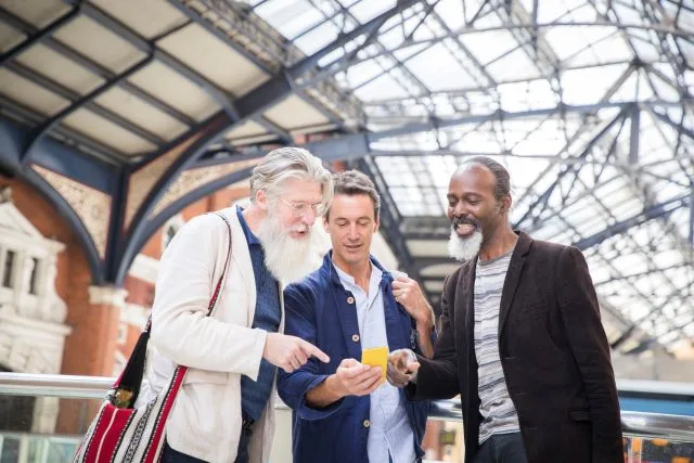Three men meet at a train station while looking at a phone screen together.