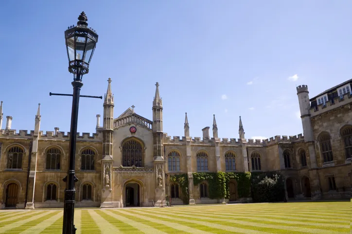 A historic university building with a manicured green lawn against a blue sky. 