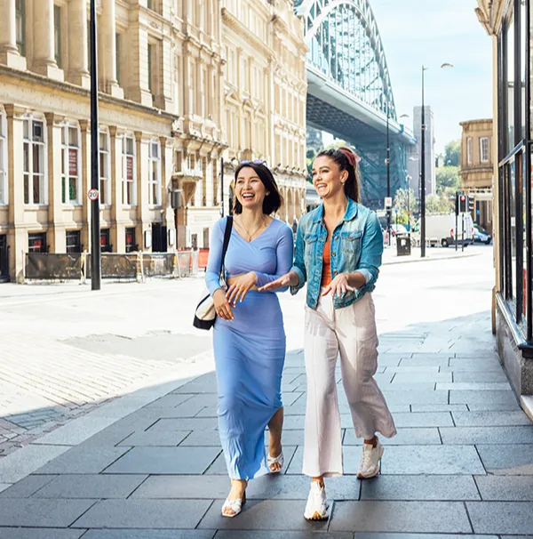 Two smiling women walking down a quiet street on a sunny day. 