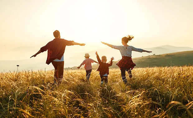 A family running through a field at sunset, seen from behind. 