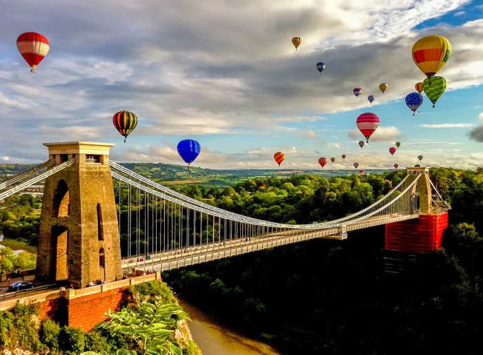 Brightly coloured air balloons fly over Clifton Suspension Bridge in Bristol crossing over the river Avon