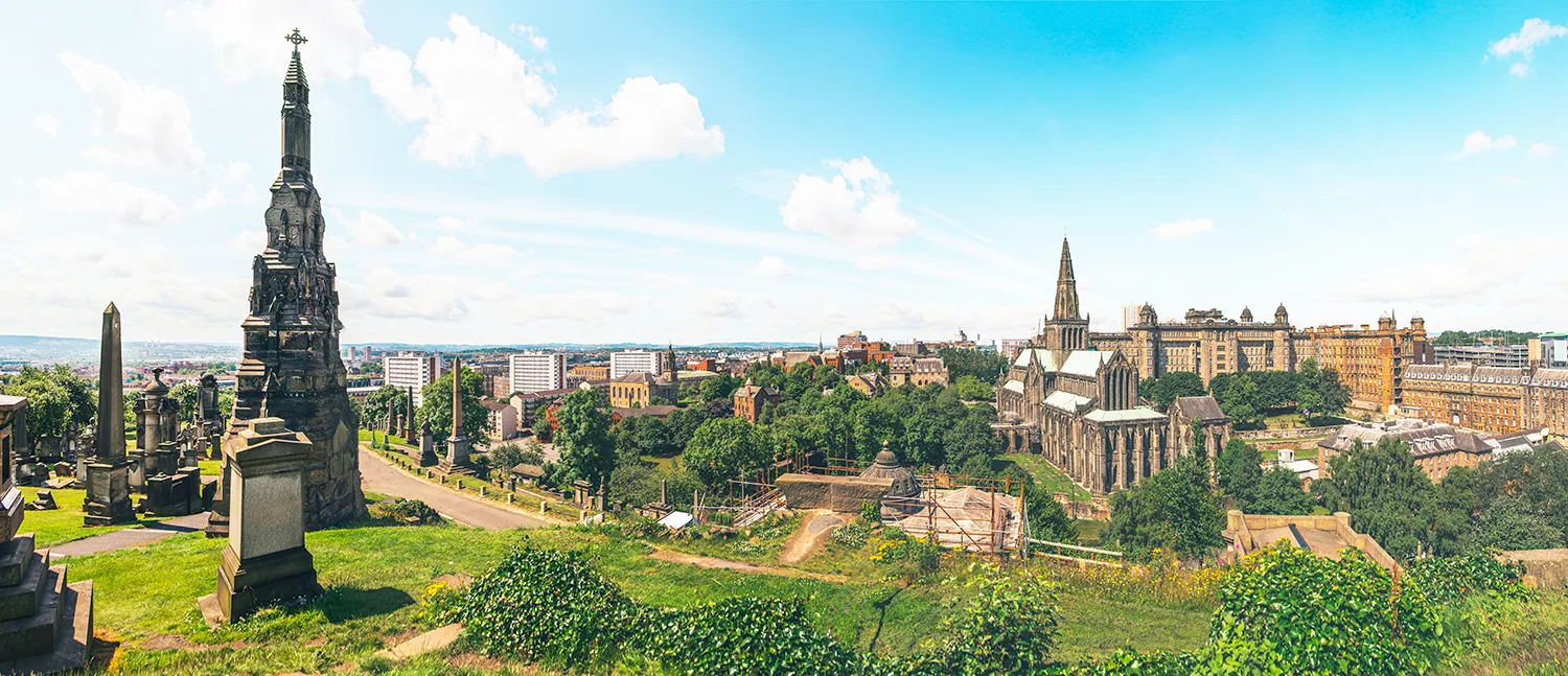 View from a cemetery on a hill overlooking a large cathedral and the city of Glasgow.