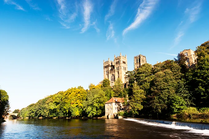 View from the river Wear looking up at Durham Cathedral's towers on a tree-lined hill.