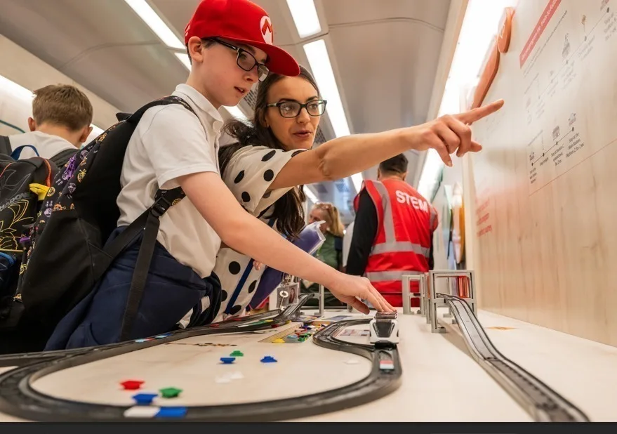 Child in red cap and adult examining a model railway display.