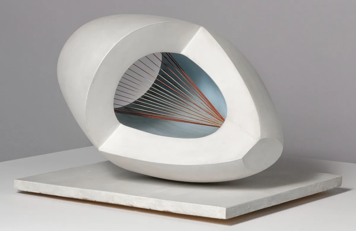 White abstract sculpture with an oval hollow interior, featuring radiating red and black strings against a pale blue surface.