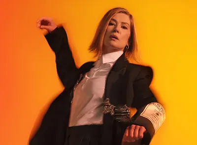 Actress Rosamund Pike, a white woman with shoulder length blonde hair, wearing a white shirt and black suit jacket. 