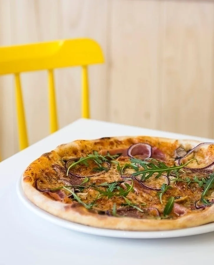 A pizza on a white table with a bright yellow chair behind. 