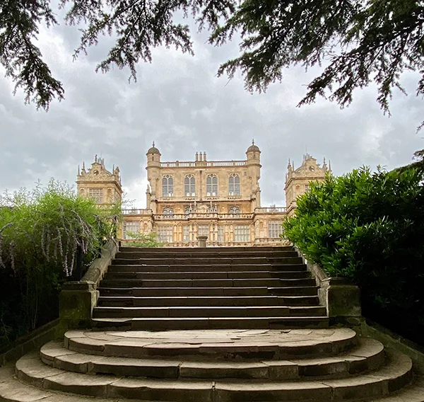 Stone steps between green bushes leading up to a huge mansion. 