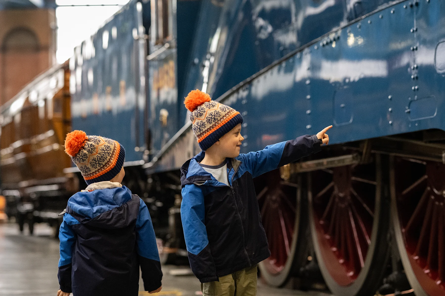 2 young white boys in matching anoraks and bobble hats looking at a vintage train