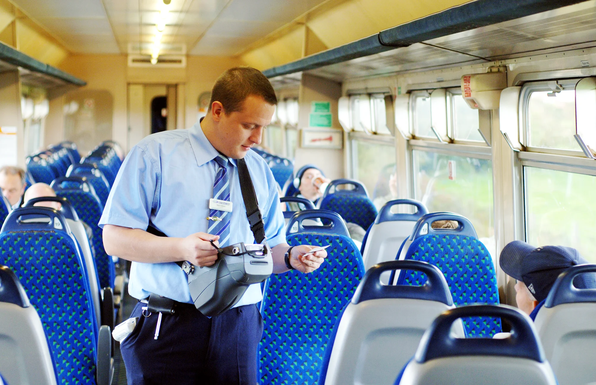 A male train revenue inspector checks a passenger's ticket onboard a train