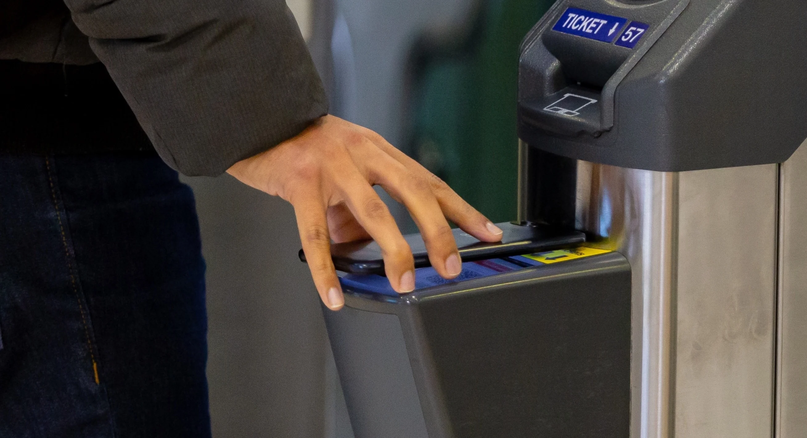 A hand scanning a smart ticket on a mobile phone at a National Rail station ticket barrier