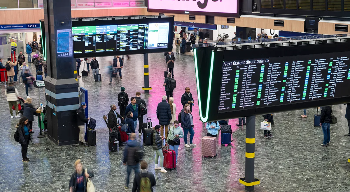 London Euston station concourse with passengers checking departure boards and walking with luggage.