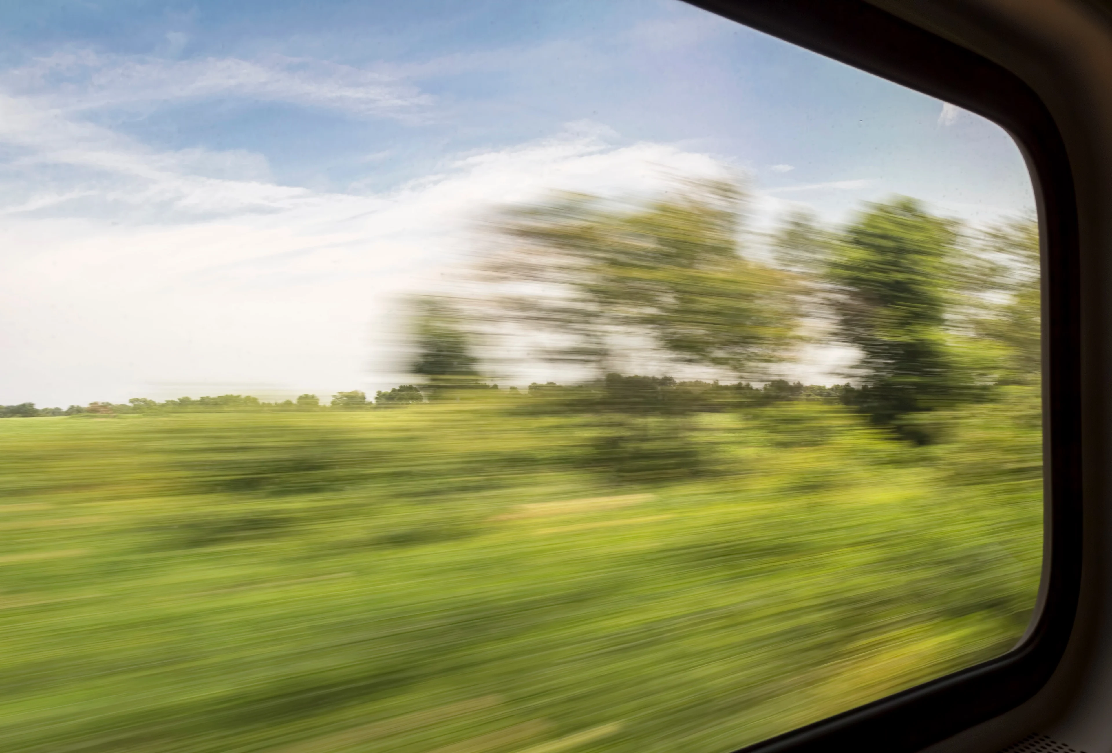 Blurred view of green fields and trees from the window of a fast-moving train
