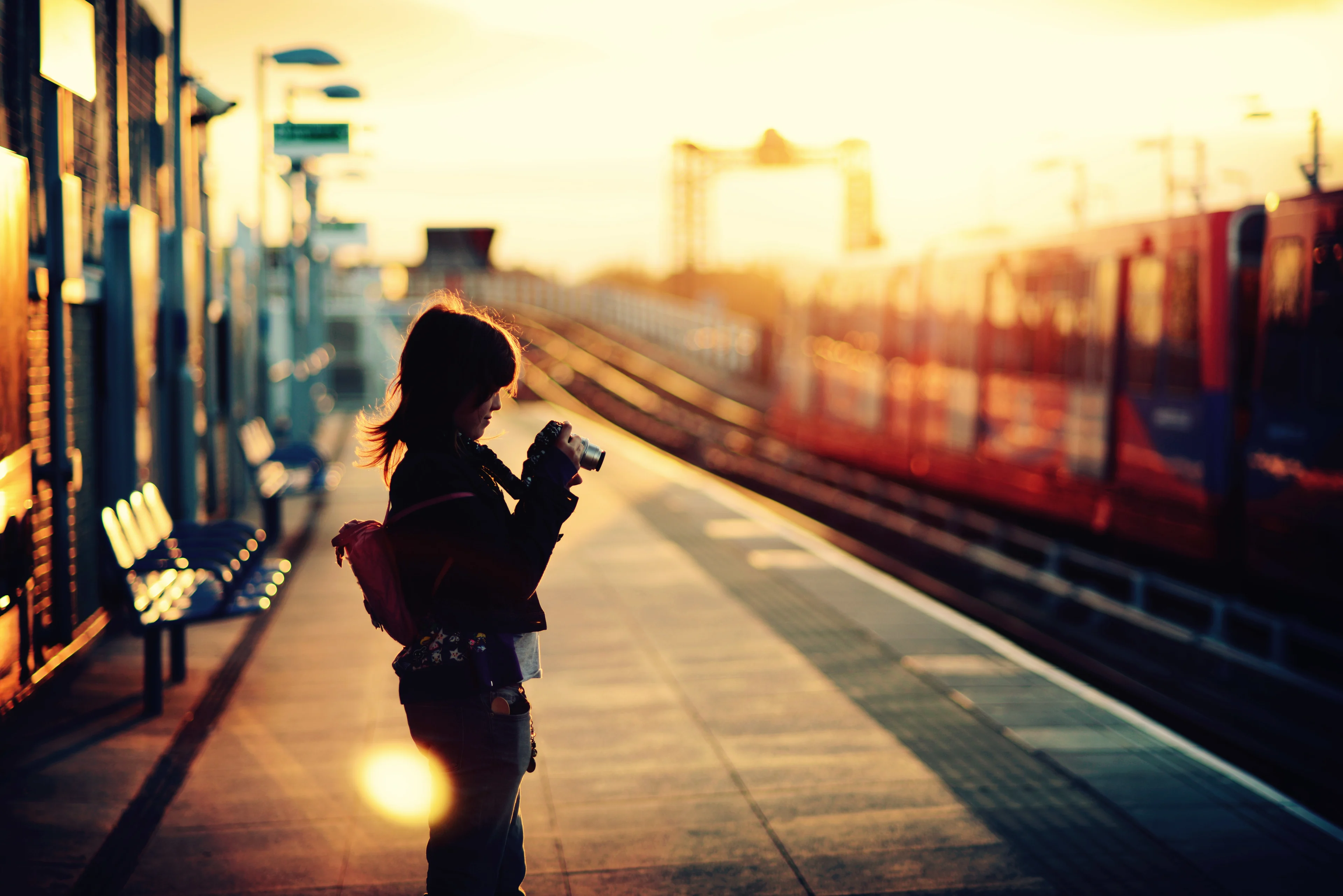 a young woman with a camera standing alone on a rail station platform at twilight