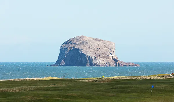 A large rocky outcrop in the sea, near to the shore. A golf course runs up to the water. 