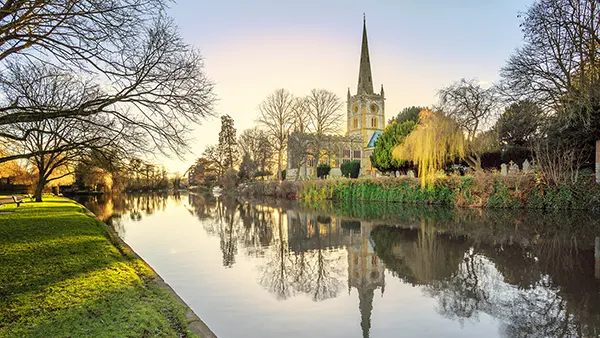 View across a tranquil river to an old church surrounded by trees. 