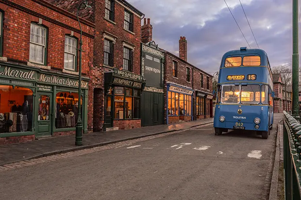 An old-fashioned blue double-decker bus drives down a street in an open air museum.