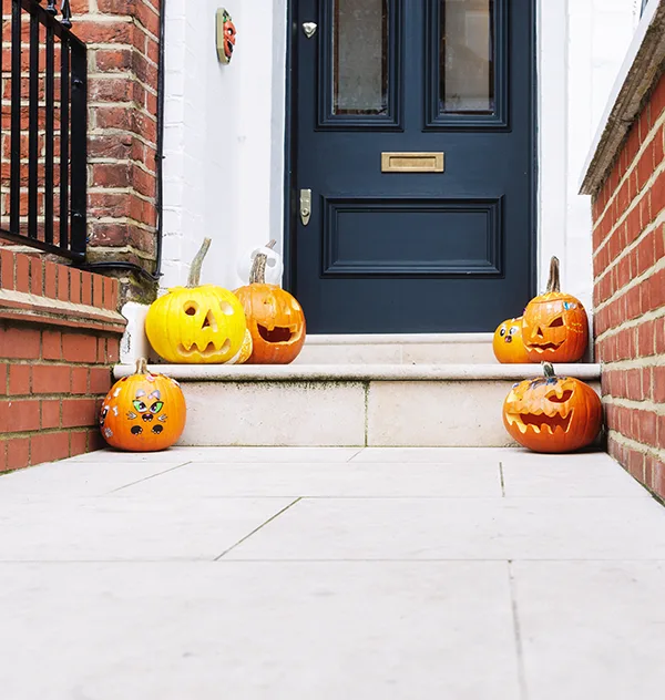 A variety of carved pumpkins sitting on the steps of a house in the daytime. 