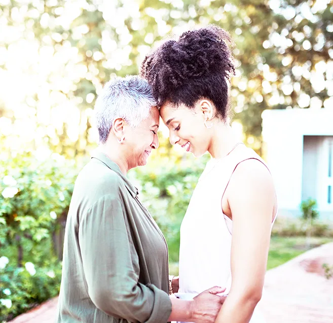 A Black woman with short grey hair smiling and being embraced by a younger smiling Black woman.