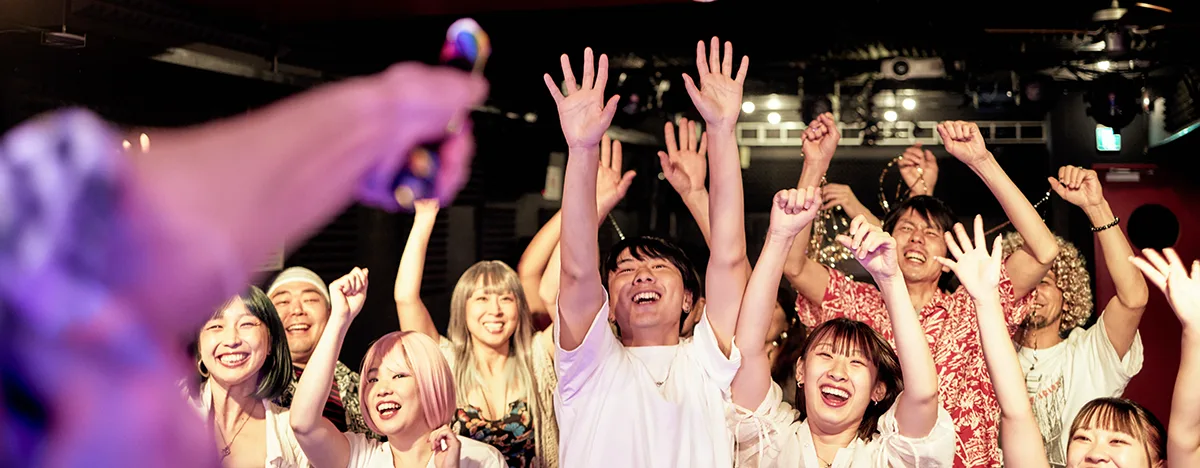 Looking into the audience at a music concert, where mostly East Asian concert-goers are smiling and waving their arms. 