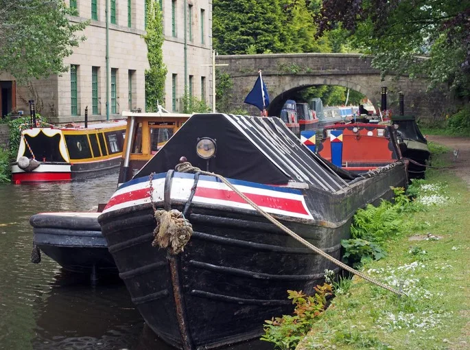 Boats on a canal next to a towpath with a stone bridge in the background. 