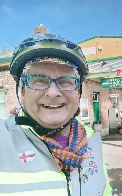 TV presenter Timmy Mellett wearing a cycle helmet and standing on a railway platform with a bicycle.