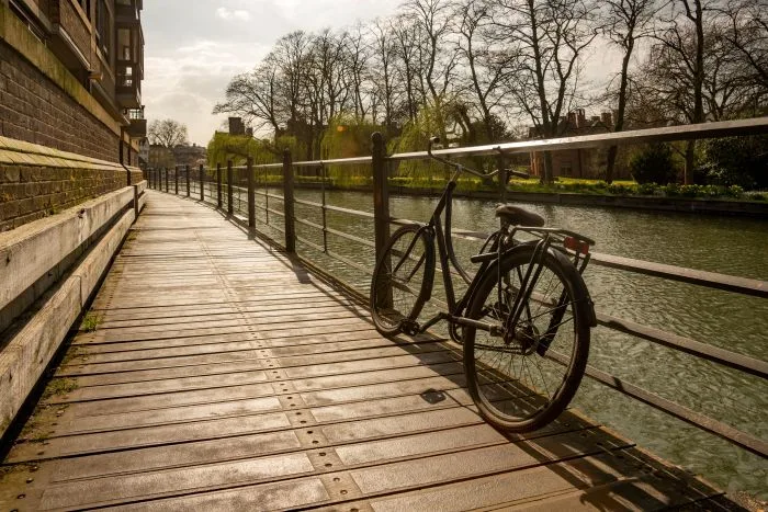 A bicycle sits against railings of a wooden pathway along a river.