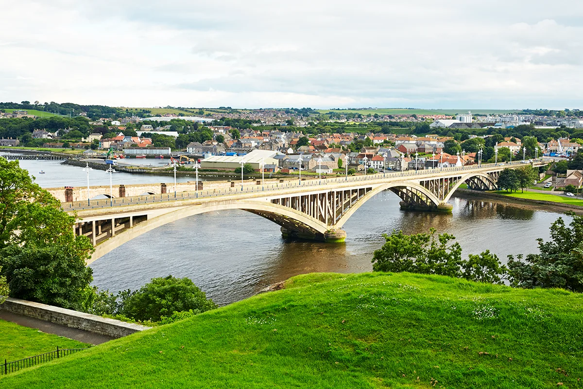 A bridge across a wide river with a picturesque village on the other side. 