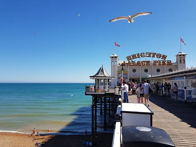 Looking down Brighton's Palace Pier, a wooden structure with shops and rides, out towards the sea on a sunny day. 