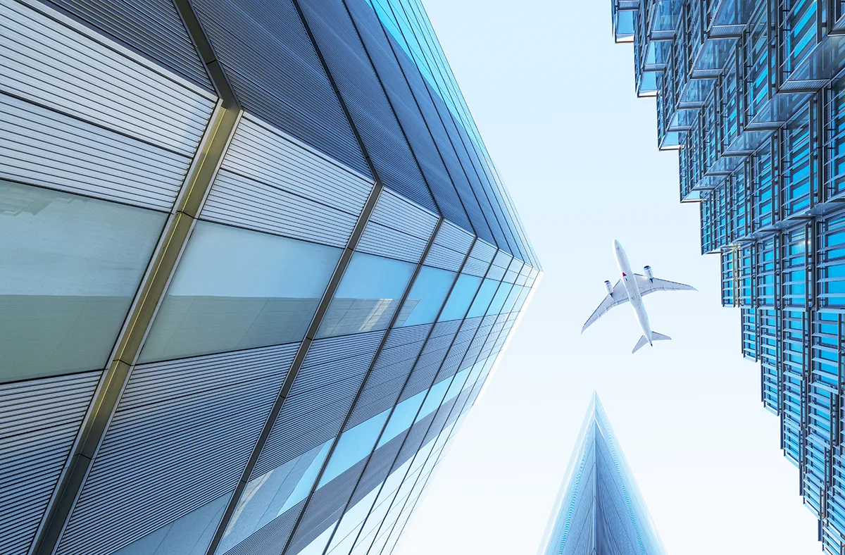 Looking up between large skyscrapers with a passenger airplane flying directly overhead. 