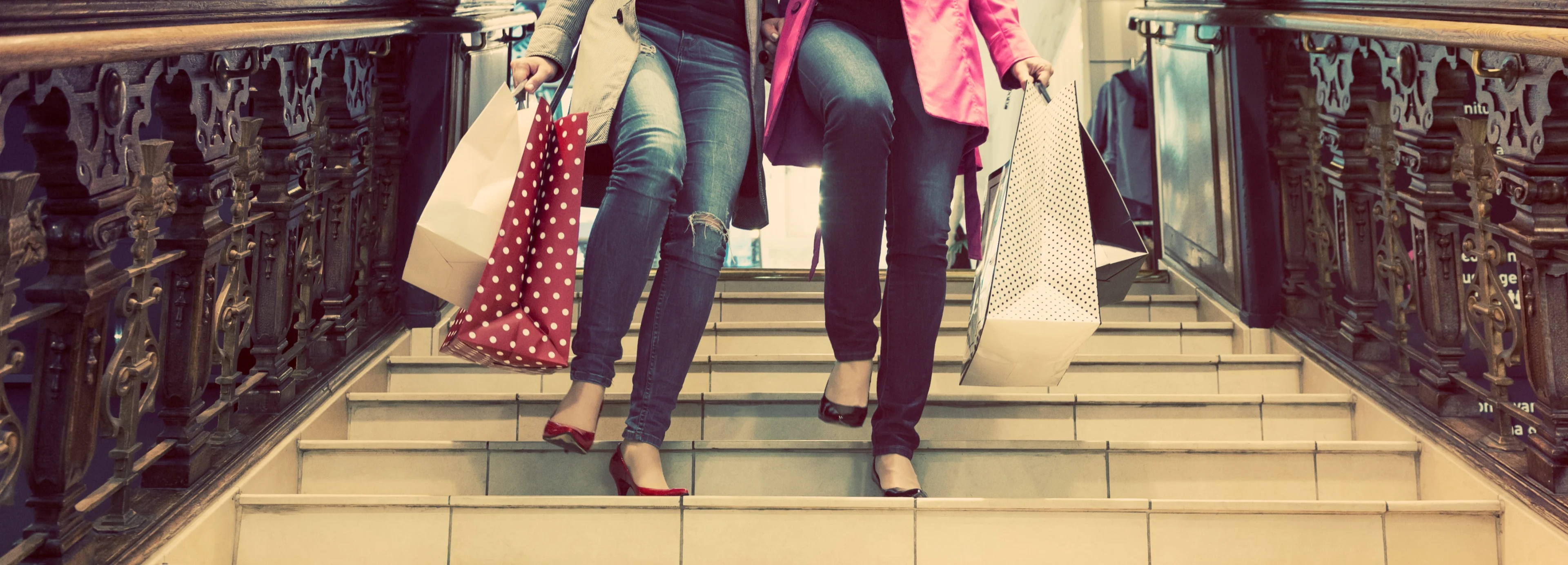 2 women carrying luxury shopping bags descend a staircase