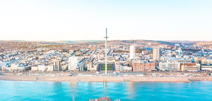 An aerial view from the sea in Brighton with the derelict West Pier and i360 tower in the foreground and the city and South Downs behind. 