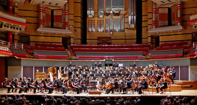An orchestra on stage in a concert hall in front of an audience.