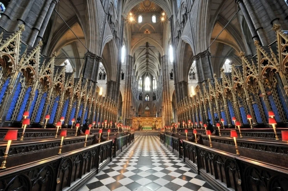 The inside of a large cathedral with black and white checked floor, wooden pulpit and high stone arches and ceiling. 