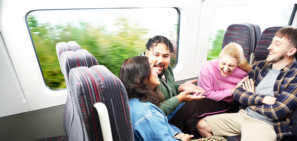 Passengers enjoying a train journey together, laughing and socialising as scenery blurs past the window.