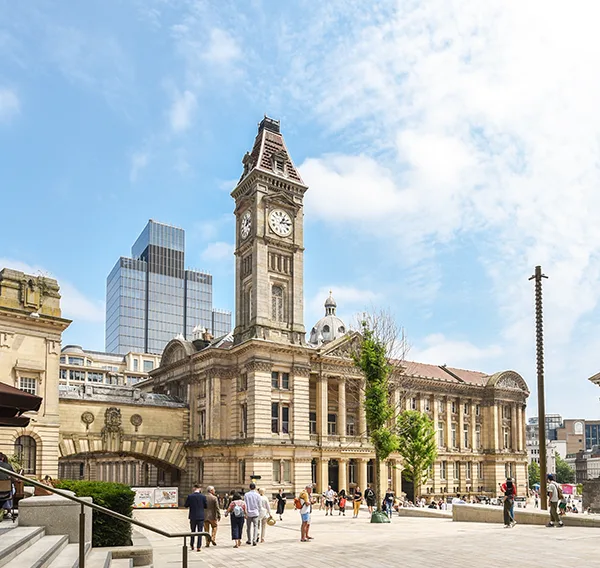 An impressive yellow stone civic building with a clock tower in a bright square on a sunny day.