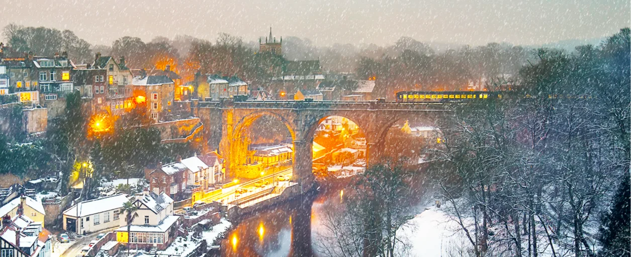 A train crossing a bridge at dusk on a snowy day.