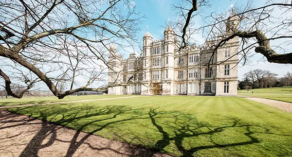 View of an imposing white stately home with shadows of winter trees across the lawn in front. 
