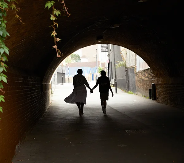 A couple in silhouette holding hands and walking through a tunnel.