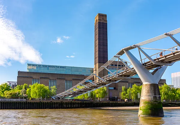 The Tate Modern art gallery with its tall chimney and the Millennium Bridge crossing the River Thames in London.