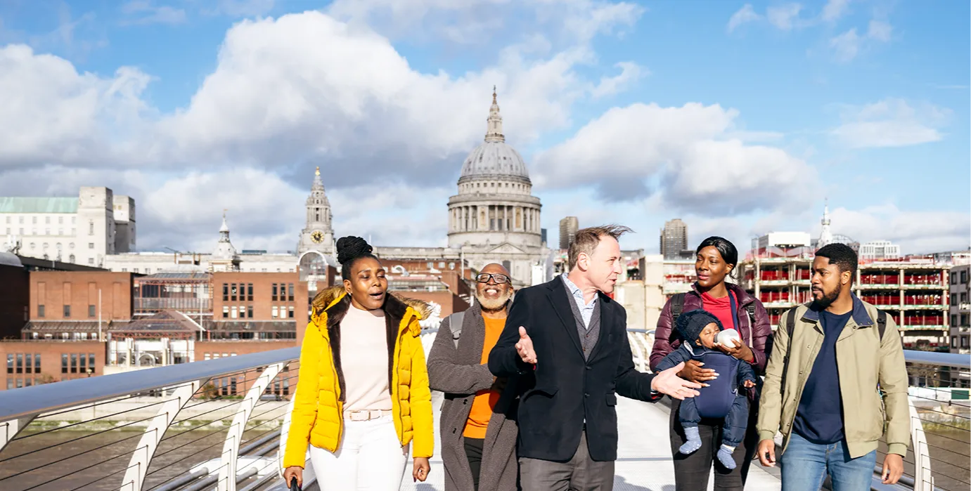A tour guide talks to 4 people on a bridge over the Thames with St Pauls cathedral in the background.