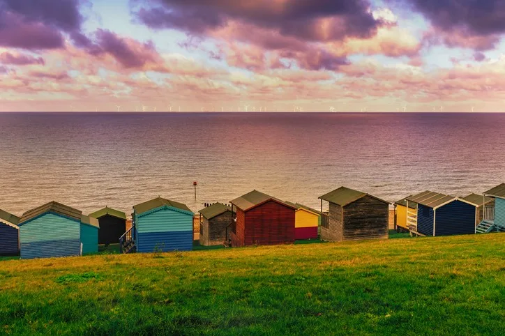 A row of colourful beach huts at dusk overlooking a calm sea. 
