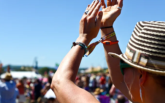 A white woman wearing a straw hat raises her hands in the air as she enjoys Glastonbury Festival on a sunny day.