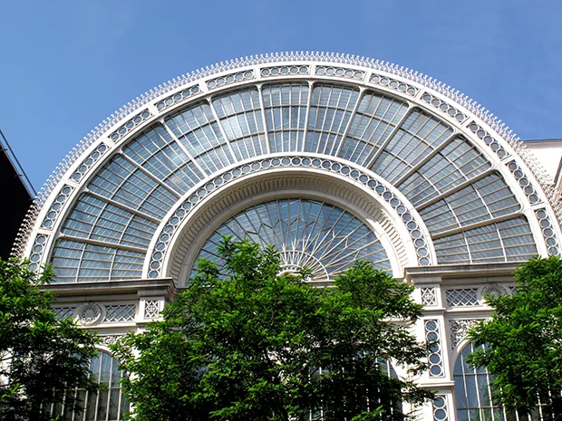 An elaborate glass-panelled building with green trees in front. 