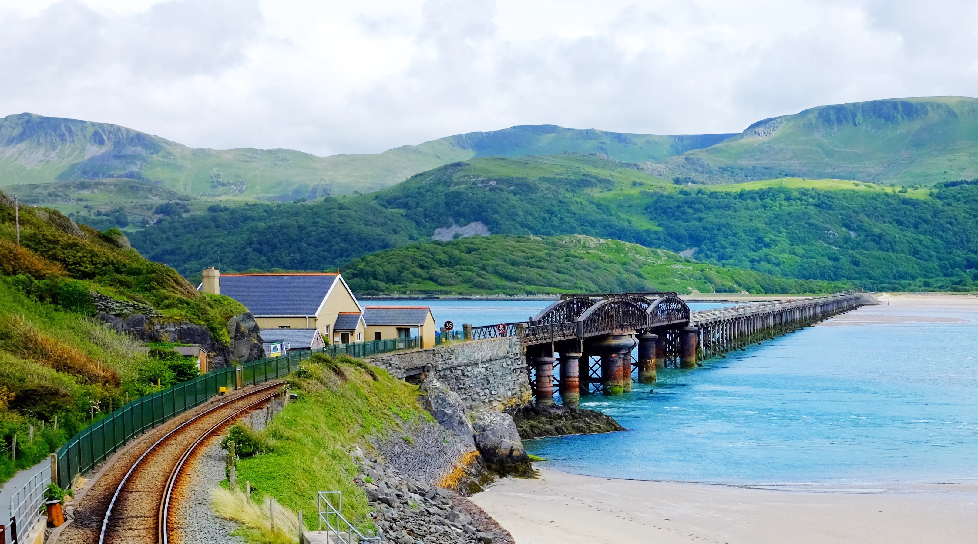 A railway bridge over a sandy beach with blue sea, with green hills in the background