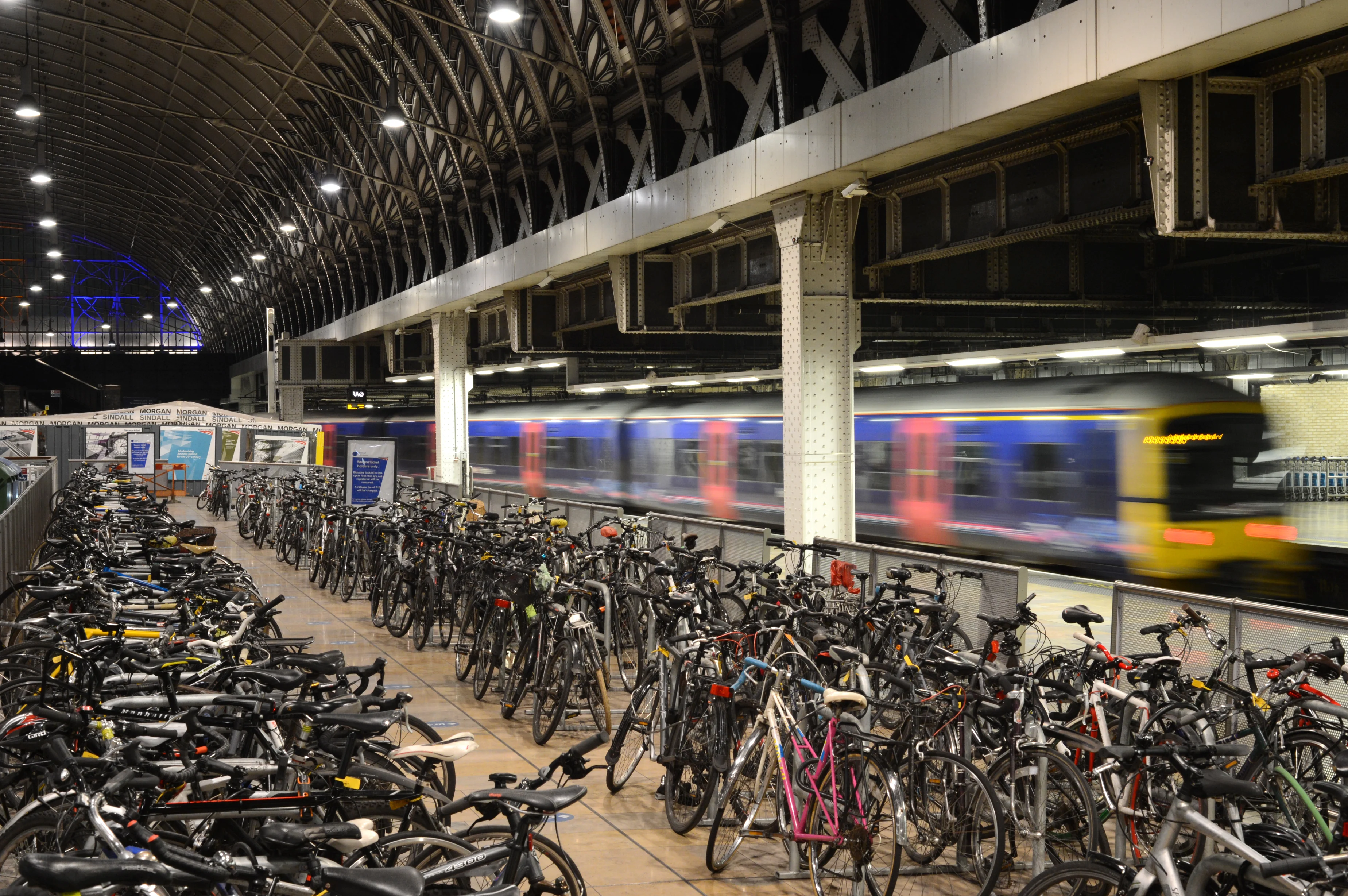 A very large bicycle parking area next to a station platform where a train is standing.