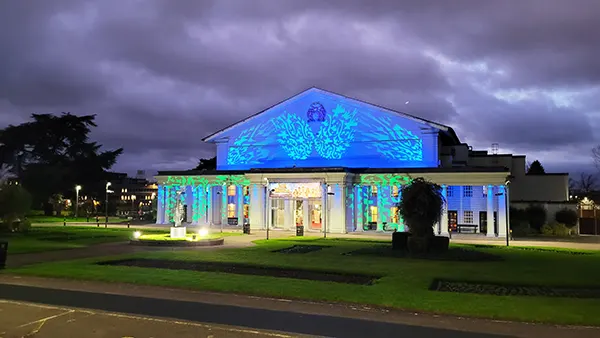 A white building at dusk with colourful images projected onto the front. 